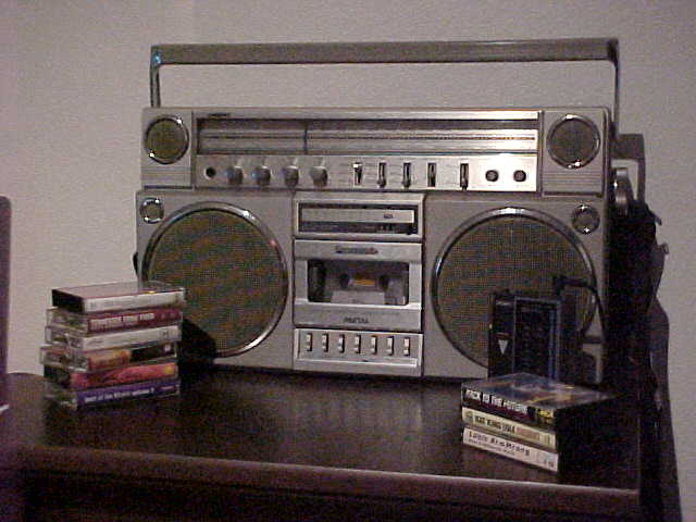 Early '80s Aiwa walkman and Panasonic boombox on a table with some cassettes.