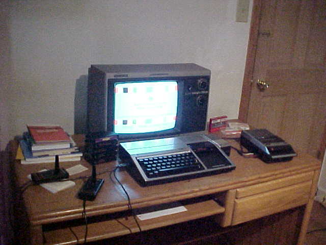 A Texas Instruments Home Computer and '80s Magnavox TV, with books, joysticks, and cartridges on one side, and on the other, a cassette recorder with TDK D-60 cassettes.