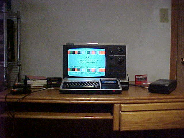 A Texas Instruments Home Computer and 70's Magnavox TV, with books, joysticks, and cartridges on one side, and on the other, a cassette recorder with TDK D-60 cassettes.