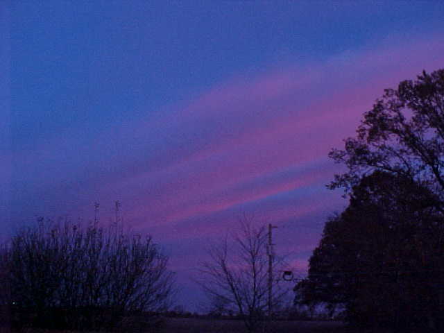 A dark blue sky with purple-tinted clouds and a landscape's silhouette.