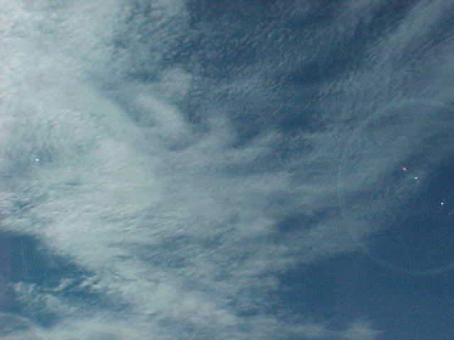 A blue sky with oddly uniform clouds and a lens flare.