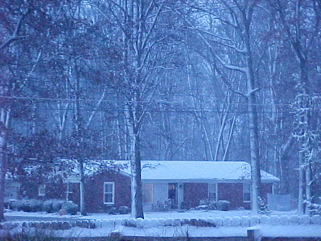 A one-story snow-covered house with a wreath on it's door in the trees.